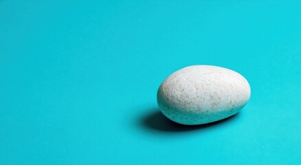 A smooth, off-white stone rests on a vibrant turquoise surface, showcasing a simple, elegant composition.
