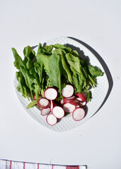 Radish slices and watercress leaves on a white plate, top view