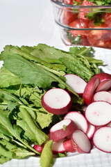 Close-up radish slices and watercress leaves on a white plate on red checkered kitchen towel, top view