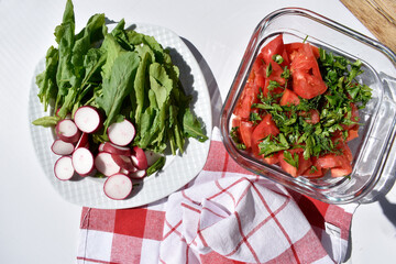 Salad made of red tomatoes and greens in a square glass dish and a plate with radish slices and lettuce leaves