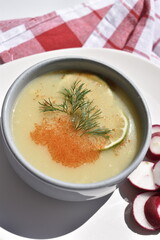 A plate of pea soup served with radish slices and lettuce leaves on a red checkered kitchen towel