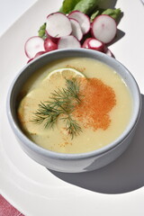 A plate of pea soup served with radish slices and lettuce leaves on a red checkered kitchen towel