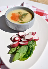 A plate of pea soup served with radish slices and lettuce leaves on a red checkered kitchen towel