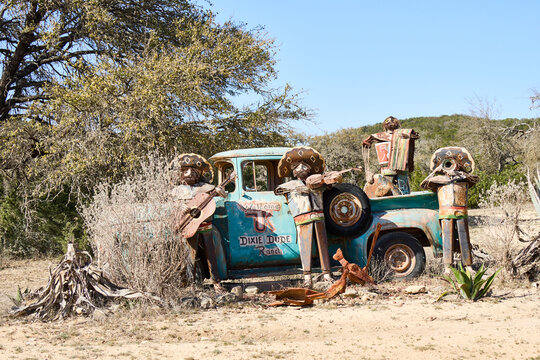 Rusty vintage truck decorated with metal mariachi sculptures at Dixie Dude Ranch in the Texas Hill Country. Artistic roadside display with desert plants