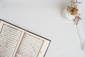 An open Quran on a white minimalist background with a dried flower in a vase, symbolizing peace, faith, and spirituality.