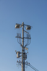 Towering Japanese utility pole bristling with insulators, cables, and transformers stands on crisp blue sky, detailing infrastructure, energy distribution, and engineering details of power networks.