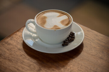 A cup of Kenyan aromatic coffee with creamy foam and scattered coffee beans on the saucer.