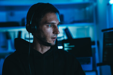Caucasian male IT engineer and programmer coding at night shift, wearing headset, working in dark office environment.