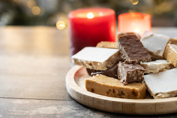 Assorted traditional Christmas nougat on wooden plate and christmas tree background. Copy space