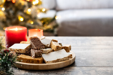 Assorted traditional Christmas nougat on wooden plate and christmas tree background. Copy space