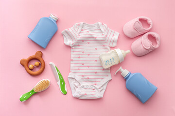 Flat lay of baby hygiene cosmetic products - shampoo and soap with a comb. Eco friendly accessories - bodysuit and wooden toys with bottle of milk on pink background, top view