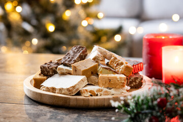 Assorted traditional Christmas nougat on wooden plate and christmas tree background