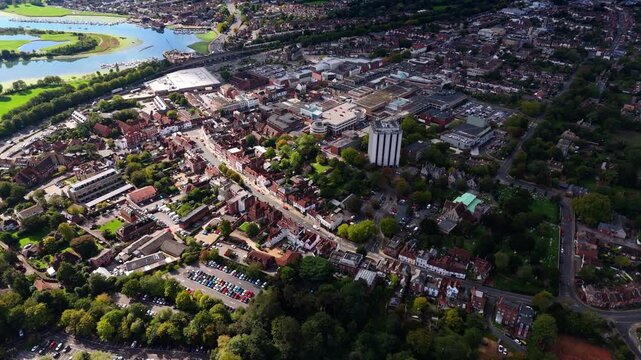 Aerial drone pans left over Fareham town centre with river and trees, showcasing cars, roads, and autumn colours glowing warmly in golden sunset light across the scenic English countryside.