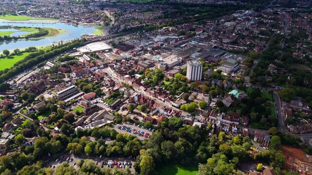 Aerial drone pans left over Fareham town centre with river and trees, capturing roads, cars, and autumn colours glowing warmly in golden sunset light across the scenic English landscape.