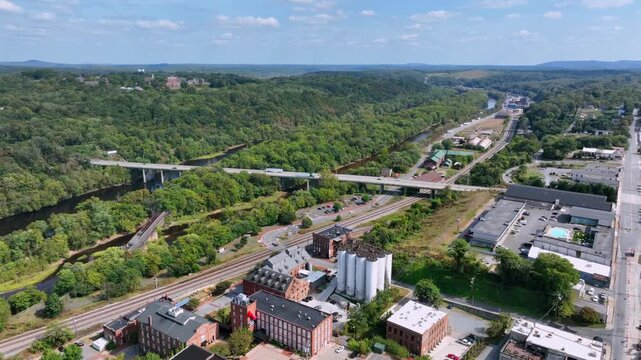 Aerial view of Lynchburg, Virginia, showing historic industrial buildings, river, bridges and surrounding green hills under clear sky. Late summer day in USA. Wide shot.