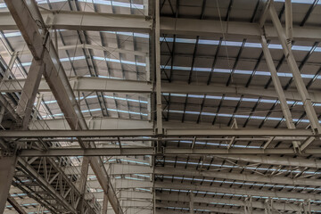 Obraz premium Interior view of industrial warehouse roof with steel beams, trusses, and skylight panels providing natural lighting. 