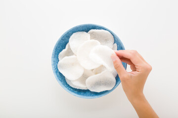 Young adult woman hand fingers taking white shrimp chips from blue plastic bowl on light gray table background. Closeup. Point of view shot. Top down view.