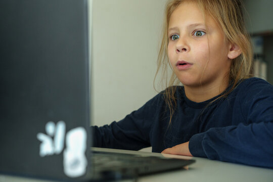 Girl studying online at home with laptop. Young schoolgirl sitting at desk with laptop, focused on online learning and doing homework. Concept of e-learning, distance education and digital skills. 