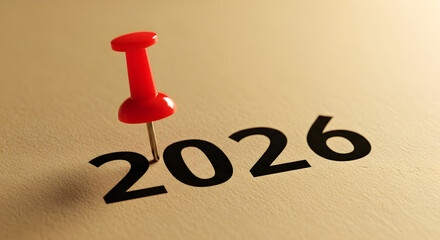 Red push pin stuck and marking the year "2026" on a calendar, planner brown paper surface 