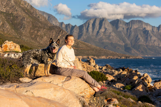 A woman with an Australian Cattle Dog (Blue Heeler) outdoors exploring together with ocean and mountain views