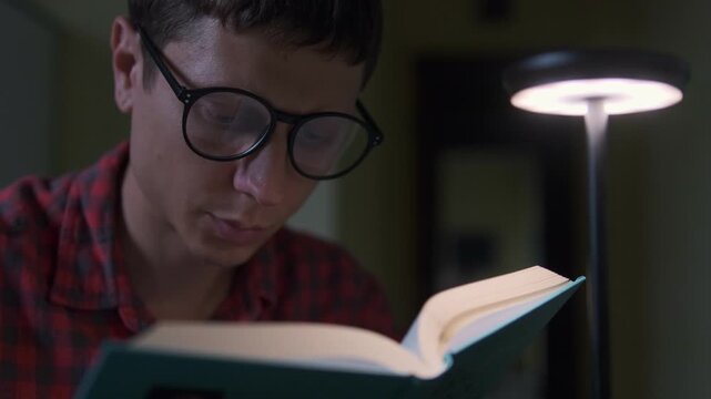 Young man reading book with desk lamp, concept of education, knowledge and self learning at home lifestyle