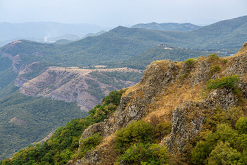 Fototapeta premium Mountain and hilly landscape. Green trees and bushes. Field with faded grass. Rock in the foreground. Azeula fortress. Kojori