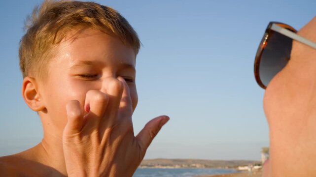 Mother tenderly applies white sunscreen to her son's smiling face in a bright day. An essential video clip on sun safety, skin care, and family health.
