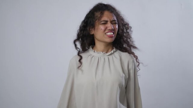 A South Asian woman with curly hair, in a light shirt, nods her head to signify "no", with a disgusted or disapproving face