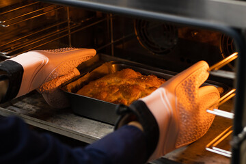 Person wearing oven mitts takes freshly baked focaccia with salt out of the oven.