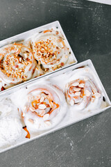 Delicious cinnamon rolls with cream cheese frosting and nuts on a dark countertop
