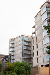 New residential complex with scaffolding on the facade and greenery in the foreground.