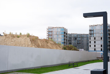 Multi-story housing under development with scaffolding and installed windows, set against a landscaped street with trees and pedestrian walkway. The image represents city growth, urban development