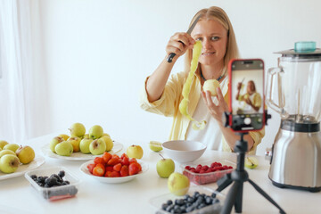 Middle-aged woman preparing homemade fruit leather, slicing fresh fruit in her kitchen for a healthy snack and streaming on her phone. Part of a series. User-generated content