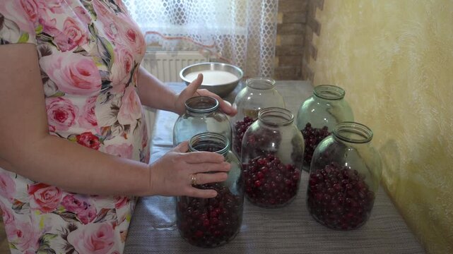 cherry compote in jars on table, housewife prepares canned compotes in jars in kitchen