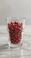 Fresh pomegranate seeds beautifully arranged in a clear drinking glass placed on a marble table surface, symbolizing natural antioxidants, healthy nutrition, refreshing superfood.