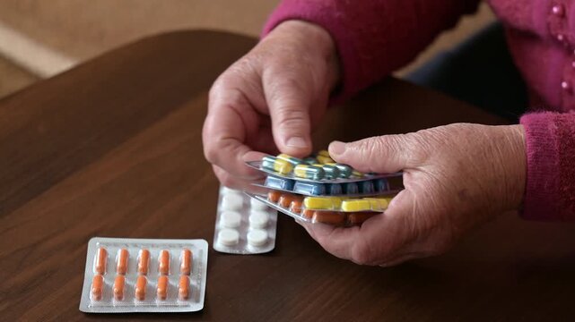 Granny organizes her daily medications at home. Elderly woman carefully collecting and sorting various pills from the table in her living room