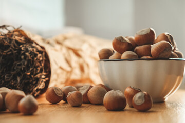 Hazelnuts are scattered across a wooden table with a clear bowl filled with them