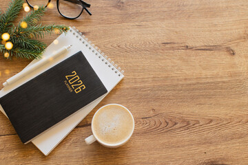 Stylish Desk Setup With 2026 Planner, Notebook, Pencil, Glasses, Fir tree Branch and Coffee on Wooden Surface