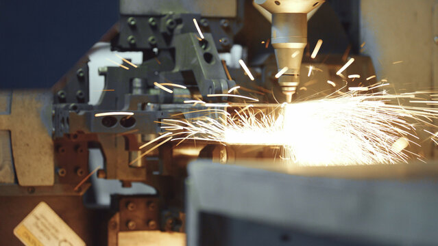Laser cutting machine nozzle emitting intense light and sparks while precisely processing a metal workpiece, illustrating modern industrial manufacturing technology and precision engineering