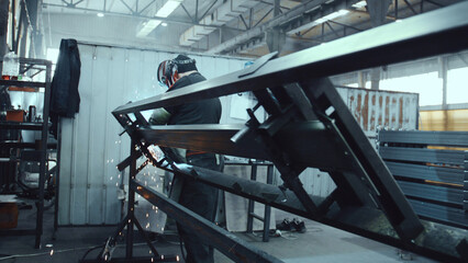 Worker fabricating a metal structure using welding equipment, illuminating sparks, a dedicated process of skilled labor and manufacturing in an industrial setting