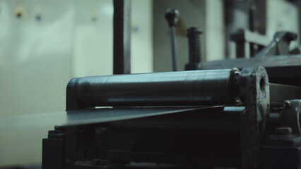Metal sheet fed through large rollers on heavy industrial machinery, close up of precision steel forming in a factory production line, highlighting modern manufacturing process