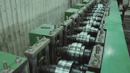 Obraz premium Industrial roll forming machine creating metal profiles, highlighting the manufacturing process and precision engineering of equipment in a factory setting
