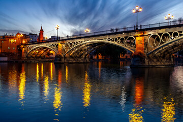 Obraz premium Dusk at Triana Bridge with glowing reflections in Seville