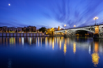 Naklejka premium Crescent moon rises over Triana Bridge at dusk in Seville