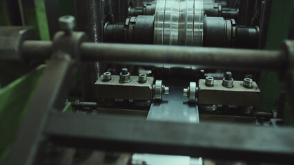 Industrial machine precisely processing a metal strip, forming it with rollers and mechanisms for manufacturing, showcasing modern factory production and mechanical engineering