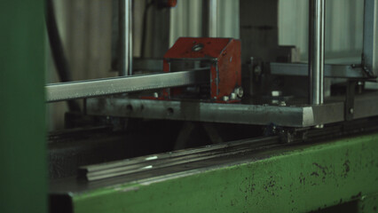 Industrial bandsaw machine precisely cutting a metal beam, demonstrating the manufacturing process of steel profiles in a factory workshop, highlighting precision metalworking and fabrication