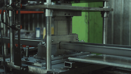 Metal profile forming machine shaping steel tubes, showcasing industrial automation, precision manufacturing, and material processing in a factory workshop environment