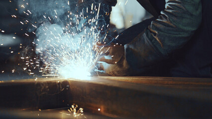 Skilled worker wearing protective gear engaging in metal fabrication, creating brilliant sparks and...