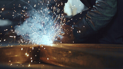 Industrial worker performing arc welding on steel beam in a manufacturing workshop, generating...