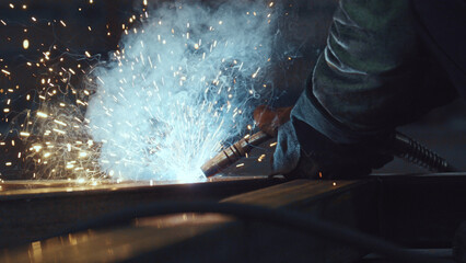 Welder wearing protective glove holding torch producing intense electric arc joining steel elements...